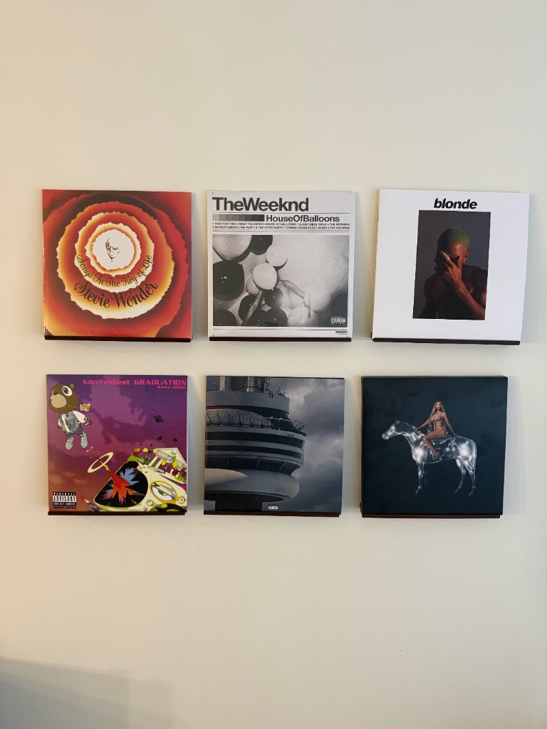 Six vinyl records on wall shelves — Stevie Wonder, The Weeknd, Frank Ocean, Kanye West, Drake, and Beyoncé